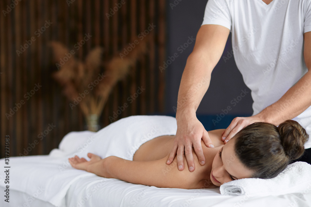 Fotografia do Stock: Young beautiful woman enjoying back and shouders  massage in spa.Professional massage therapist is treating a female patient  in apartment.Relaxation,beauty,body and face treatment concept.Home massage.  | Adobe Stock