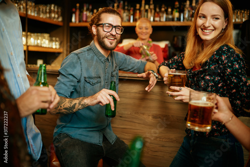 A small group of best friends standing at a pub  drinking beer  chatting and having fun. Focus on bartender wiping drinking glass. Nightlife.