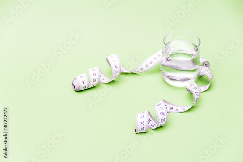 Measuring tape with glass of water on green background. Diet concept.Free copy space.