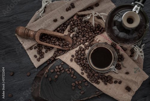 Coffee style, Cup of coffee and coffee beans roating with old wooden scoop and coffee beans around on the wooden and dark stone background.