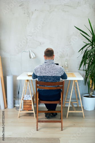 Back view of an Attractive freelance male sitting in modern office and typing on notebook.