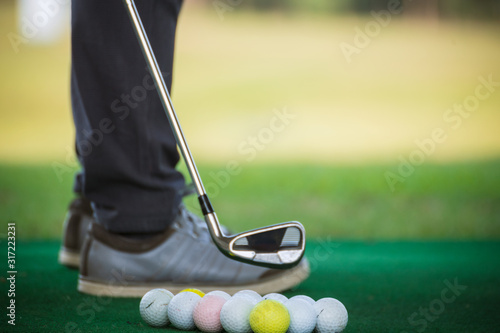 Many golf balls at golf pitch with blurred golfers feet as background.