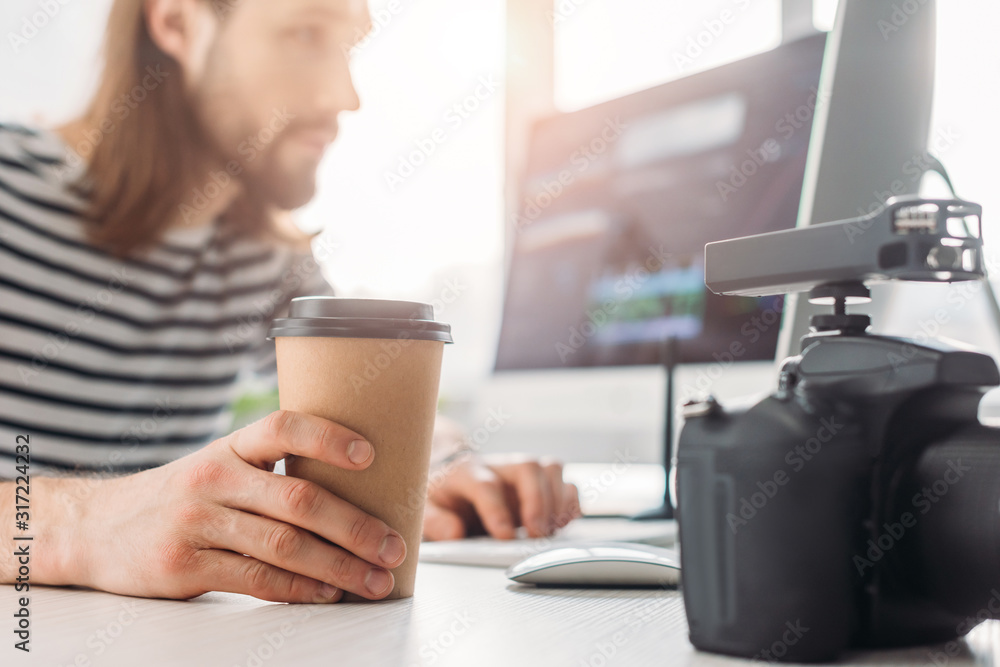 selective focus of editor holding paper cup and looking at computer monitor selective focus of editor holding paper cup and looking at computer monitor