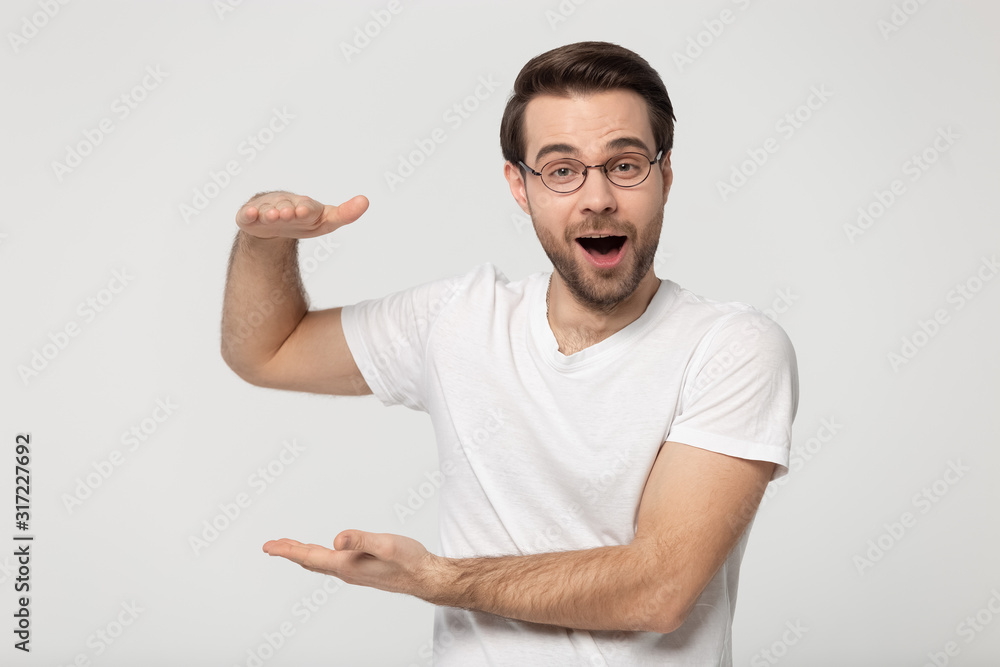 Amazed surprised millennial guy showing big size measurement. Amazed surprised millennial guy showing big size measurement.