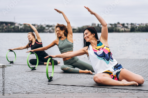 A group of sporty women doing stretching exercises with a special sports circle on the street near the water. Active lifestyle