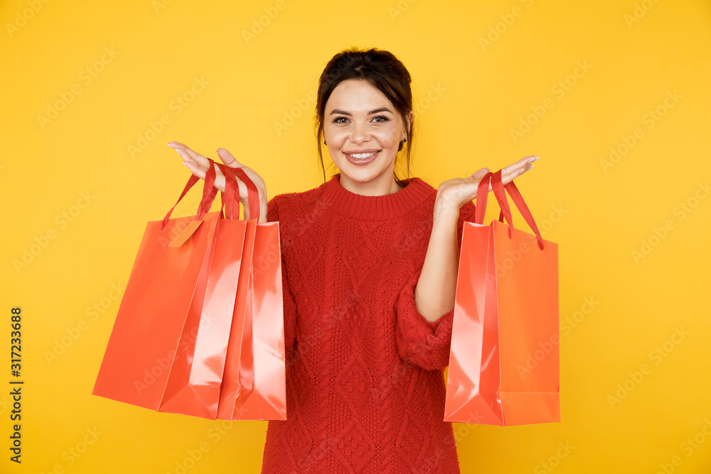 Happy young lady in the red sweater with shopping bags in the yellow studio Happy young lady in the red sweater with shopping bags in the yellow studio