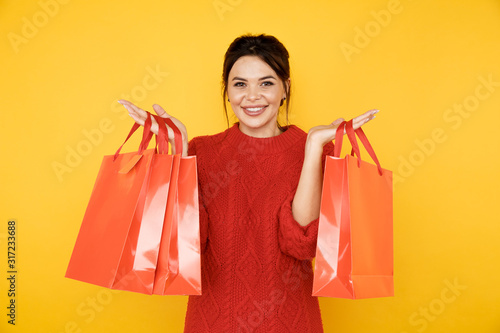 Happy young lady in the red sweater with shopping bags in the yellow studio