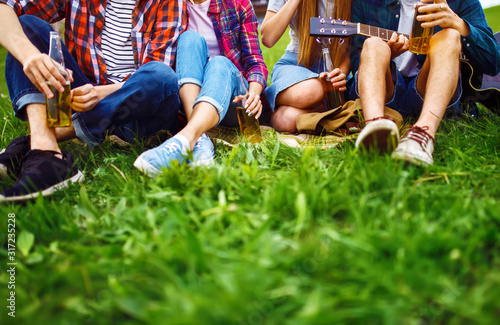 Fototapeta Naklejka Na Ścianę i Meble -  Happy friends spending free time together in park sitting on grass, drinking beer and chatting. Group of young people enjoying party n the summer park. Rest, fun, summer concept.