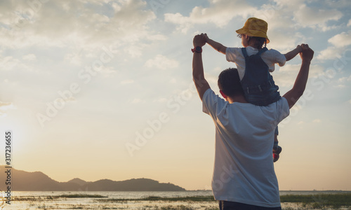 Asian daughter rode the father's neck and looked ahead together on sunset, Dad and baby girl playing together near the lake.