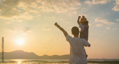 Asian daughter rode the father's neck and looked ahead together on sunset, Dad and baby girl playing together near the lake.