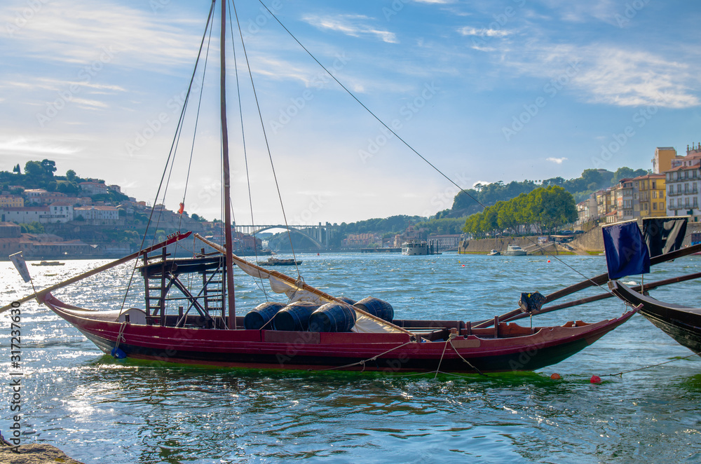 Fototapeta premium Portugal, Porto in summer, panoramic view of Douro river, red wooden boat with wine port barrels close-up, the banks of the river Douro