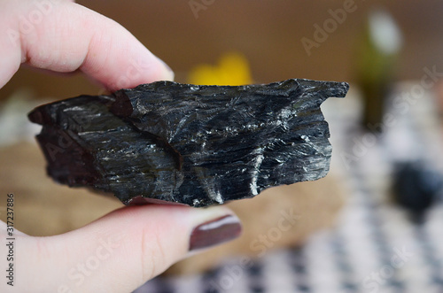 Large black healing crystal being held in woman's hand. Beautiful shiny healing jet. Jet crystal, rough jet. Natural black crystal in hand. Natural lighting, witches healing. Witchy crystals for alter