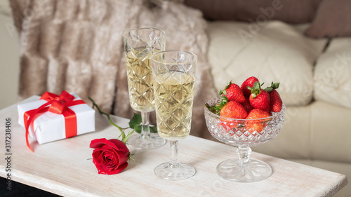 Two Champagne glasses  strawberry  red rose flower  and gift box with bow on the table in living room. Romantic date concept or Saint Valentines day celebration.