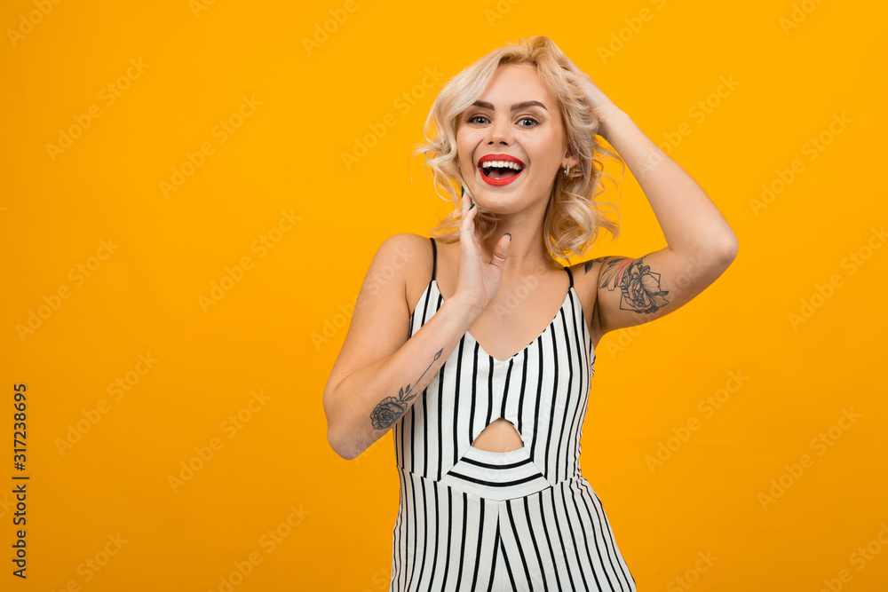 Beautiful young woman with short blonde curly hair and bright makeup gesticulated and smiles, portrait isolated on orange background