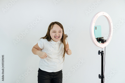 A teenage girl dances and shoots a video. Selfies. The phone is mounted on a tripod and the ring lamp shines