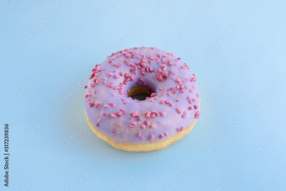Delicious bright juicy purple one sprinkled donut for a sweet tooth on a blue background. Close-up selective focus. Top view, unhealthy baked goods with sugar. Delicious bright juicy purple one sprinkled donut for a sweet tooth on a blue background. Close-up selective focus. Top view, unhealthy baked goods with sugar.