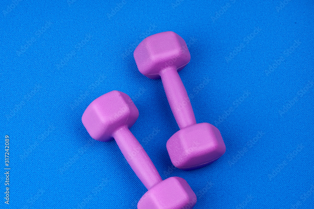pair of purple plastic dumbbells on a blue neoprene mat pair of purple plastic dumbbells on a blue neoprene mat
