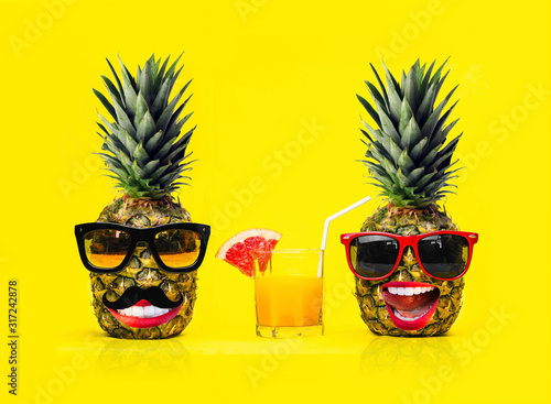 Two Fun Fashion pineapples with sunglasses and a mustache with fresh tropical smoothie with fruits on a yellow background. Husband and wife. Boy and girl.