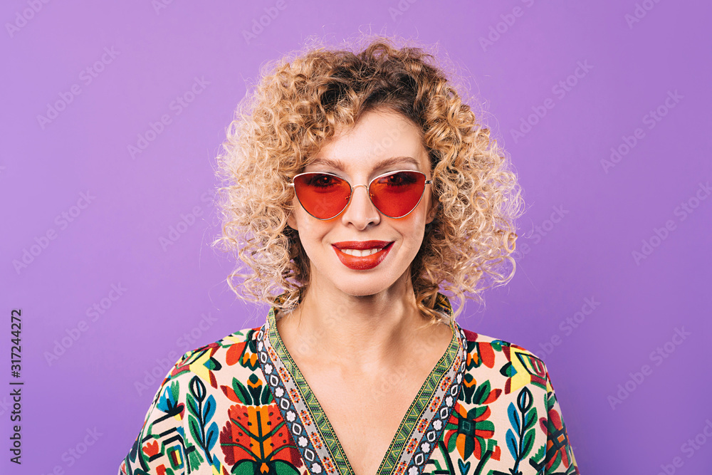 Portrait of a woman in stylish pink glasses and a curly hairstyle on a violet background. Beautiful smile on the face of a beautiful woman