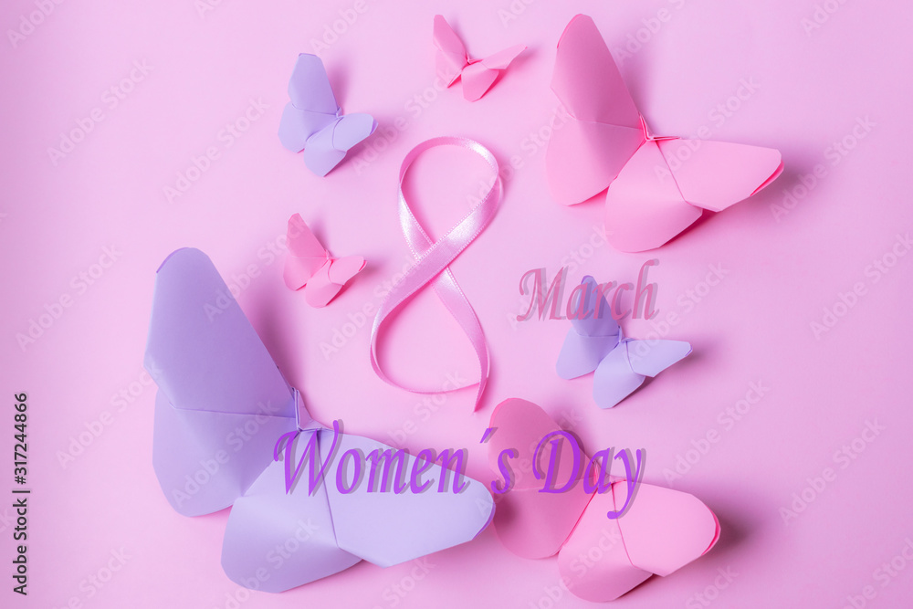 Happy Women's Day. Pink bow in the shape of 8 surrounded by pink and violet paper butterflies on isolated pink background and text Happy Women's Day, with nostalgic touch.