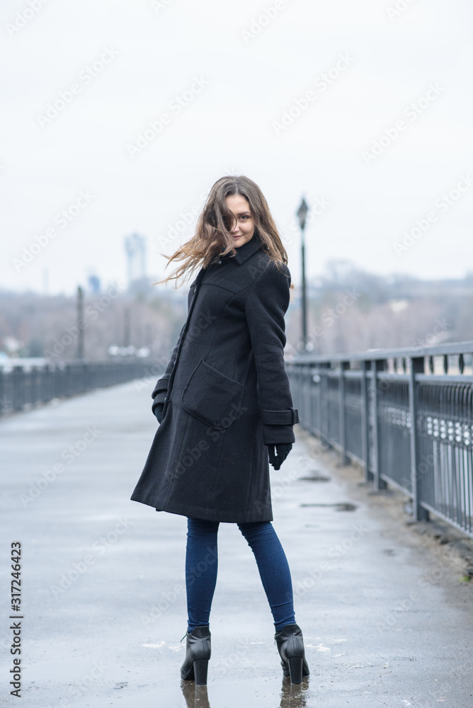 A brunette girl in a black coat is walking on a cold winter day without snow. Portrait of a girl.