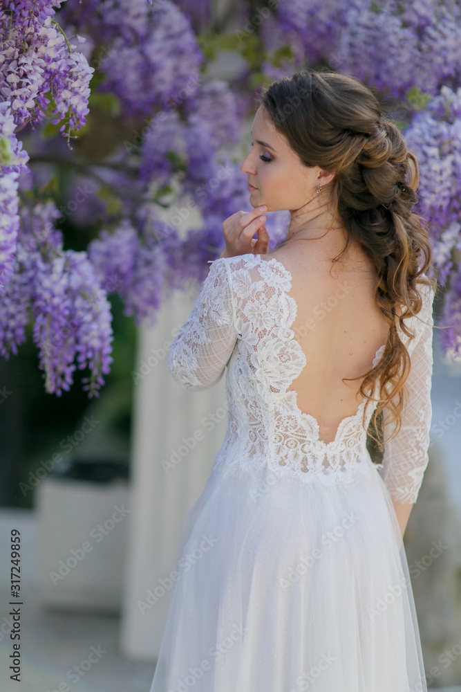 A bride in a wedding dress stands with her back to the camera under a tree. A bride in a wedding dress stands with her back to the camera under a tree.