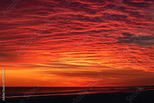 Afterglow burn in the sky after a vibrant red and pink sunset over a beach. Jones Beach New York.  photo