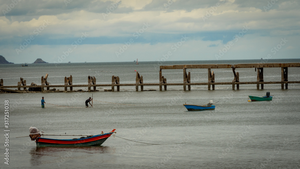 Two fishermen in water surrounded by pier and Fishing boats at Pak Nam Pram, Thailand