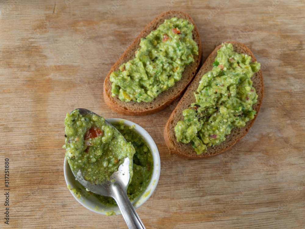 Top view on small cup and spoon with guacamole next to sandwiches lying on a wooden table Top view on small cup and spoon with guacamole next to sandwiches lying on a wooden table