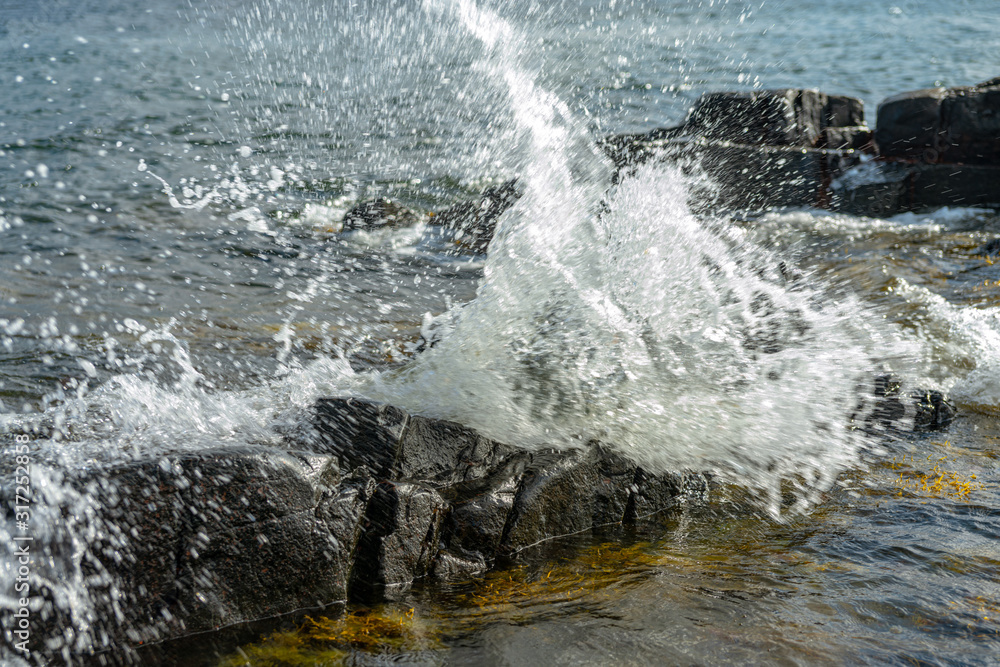 Waves splashing against rocks at the shore in sunlight