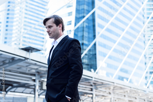 Portrait images of Cauacsian business man are standing on train station with blur tail building background, to people concept.