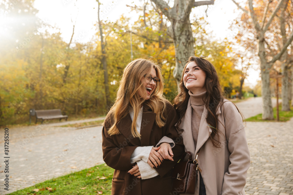 Two cheerful young pretty girls wearing coats walking together Two cheerful young pretty girls wearing coats walking together