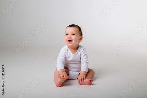 Bild auf Leinwand baby boy 9 months in a white bodysuit sitting on a white background, space for t