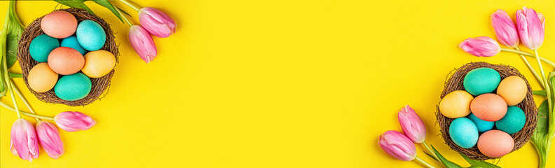 Stylish background with colorful easter eggs isolated on yellow background with pink tulip flowers. Flat lay, top view, mockup, overhead, template