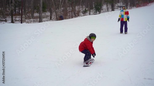 Young man snowboard instructor tiches little boy how to ride a snowboard. Winter activities concept. Slowmotion shot photo