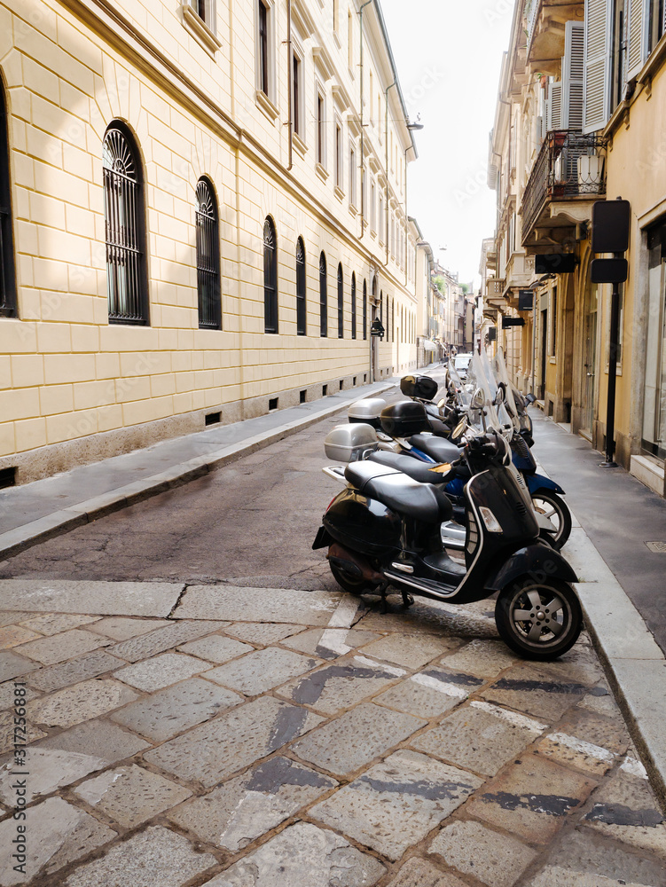 The narrow street of the old medieval city of Italy, the beautiful architecture of the houses. Scooter parking.