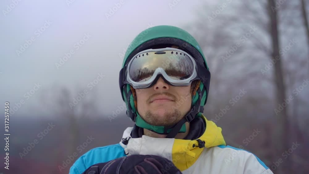Closeup shot of a young man wearing a snow googles looks at a hillside. Winter holidays concept. Slowmotion shot
