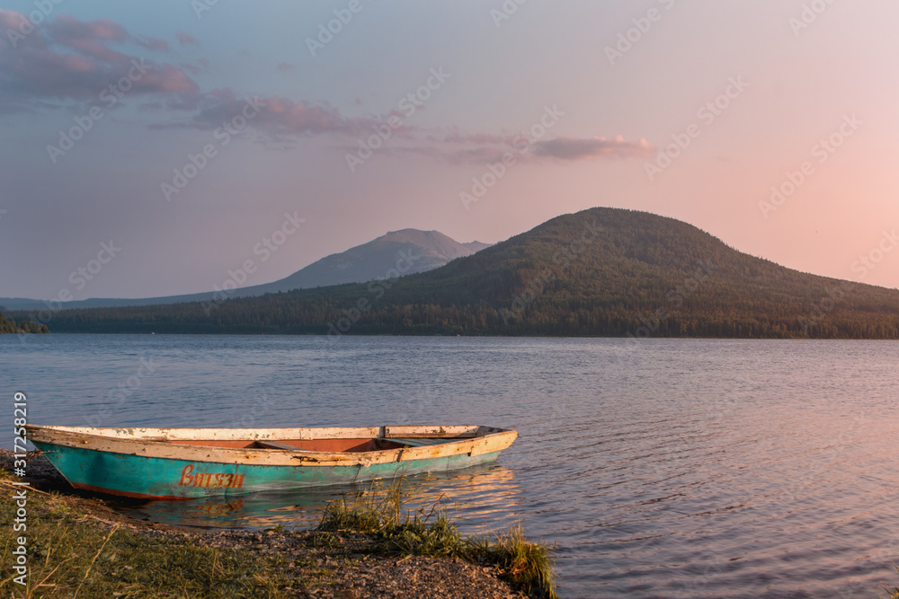 boat at the shore on the lake in the mountains at purple sunset with sun shining and reflecting in the water