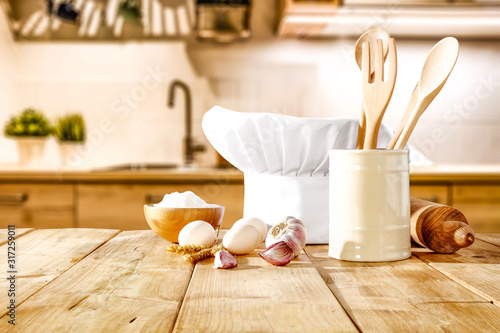 Brown kitchen furniture with empty space on table.Copsy space and kitchen board.White cook hat and few kitchen utensils.Free space for your product and morning time.  photo