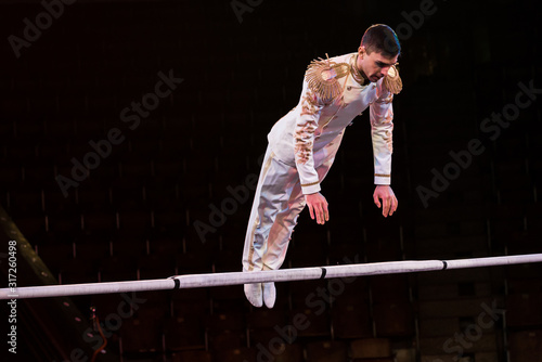 handsome gymnast exercising near pole in arena of circus