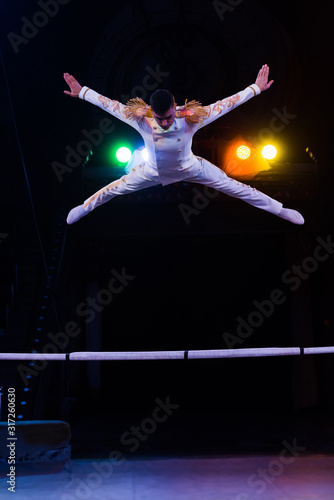 handsome gymnast in costume jumping near pole in arena of circus