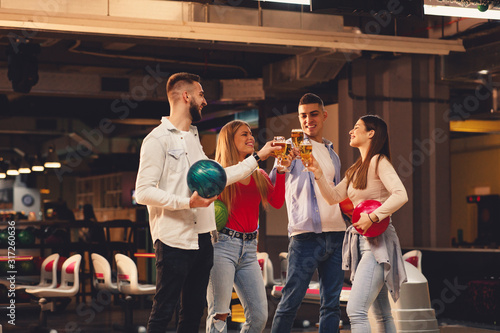 Tela Group of friends toast with a beer in a bowling alley