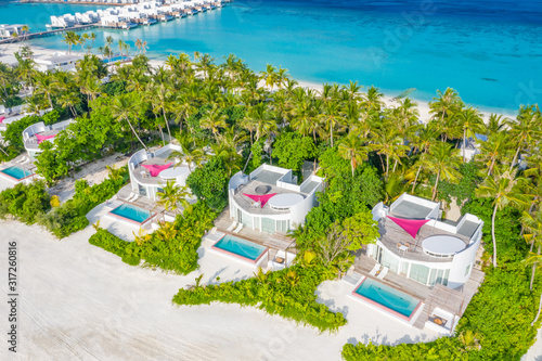 Maldives coastline, aerial landscape of luxury villas with white sand and palm trees. Paradise island aerial view, amazing blue sea and luxury vacation background