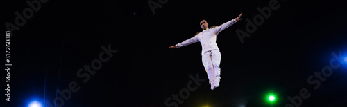 panoramic shot of handsome air acrobat with outstretched hands in arena of circus