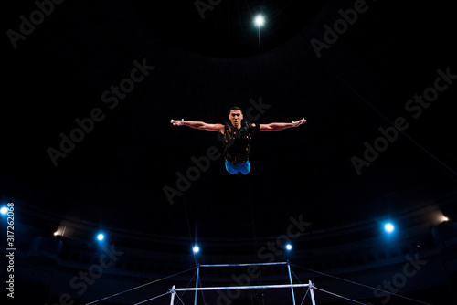 athletic gymnast with outstretched hands in arena of circus
