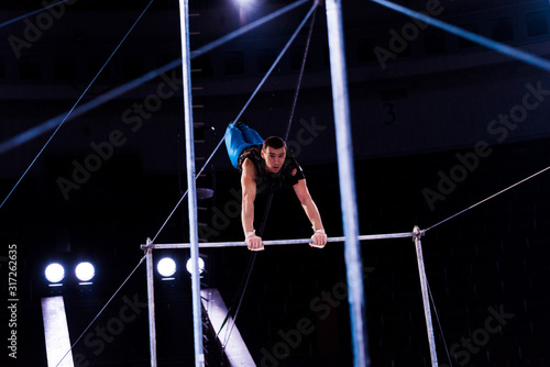 selective focus of athletic gymnast performing on horizontal bars in arena of circus