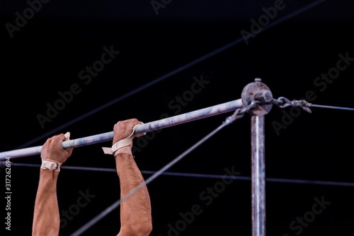 cropped view of athletic gymnast performing on horizontal bars in circus