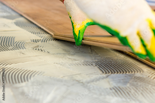 Master smears the glue on the concrete floor and lays the parquet. High-quality repair of the floor covering.