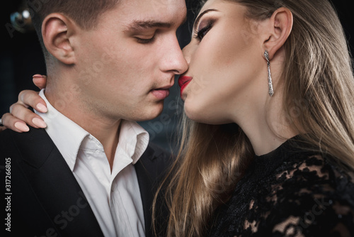 Closeup of stylish elegant young couple kiss in evening dress and suit on black background