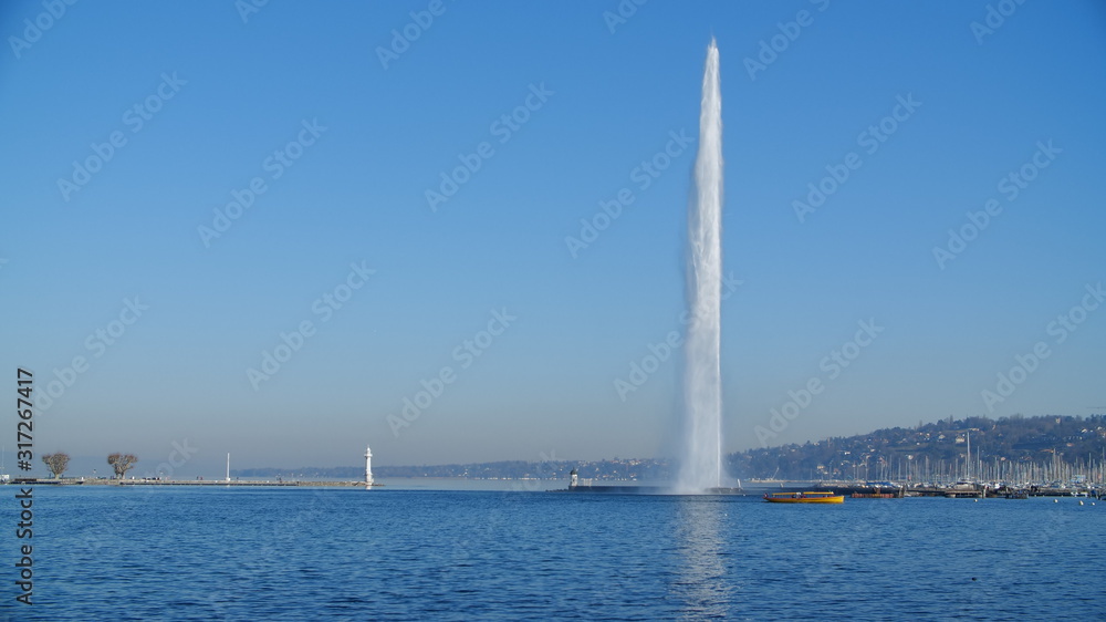 Jet d'Eau (water-jet) in full force on Lake Geneva Switzerland, taken on a clear day, perfect blue wintery skies. Postcard worthy image, capturing Genève's main attraction with small shuttle boat bus Jet d'Eau (water-jet) in full force on Lake Geneva Switzerland, taken on a clear day, perfect blue wintery skies. Postcard worthy image, capturing Genève's main attraction with small shuttle boat bus
